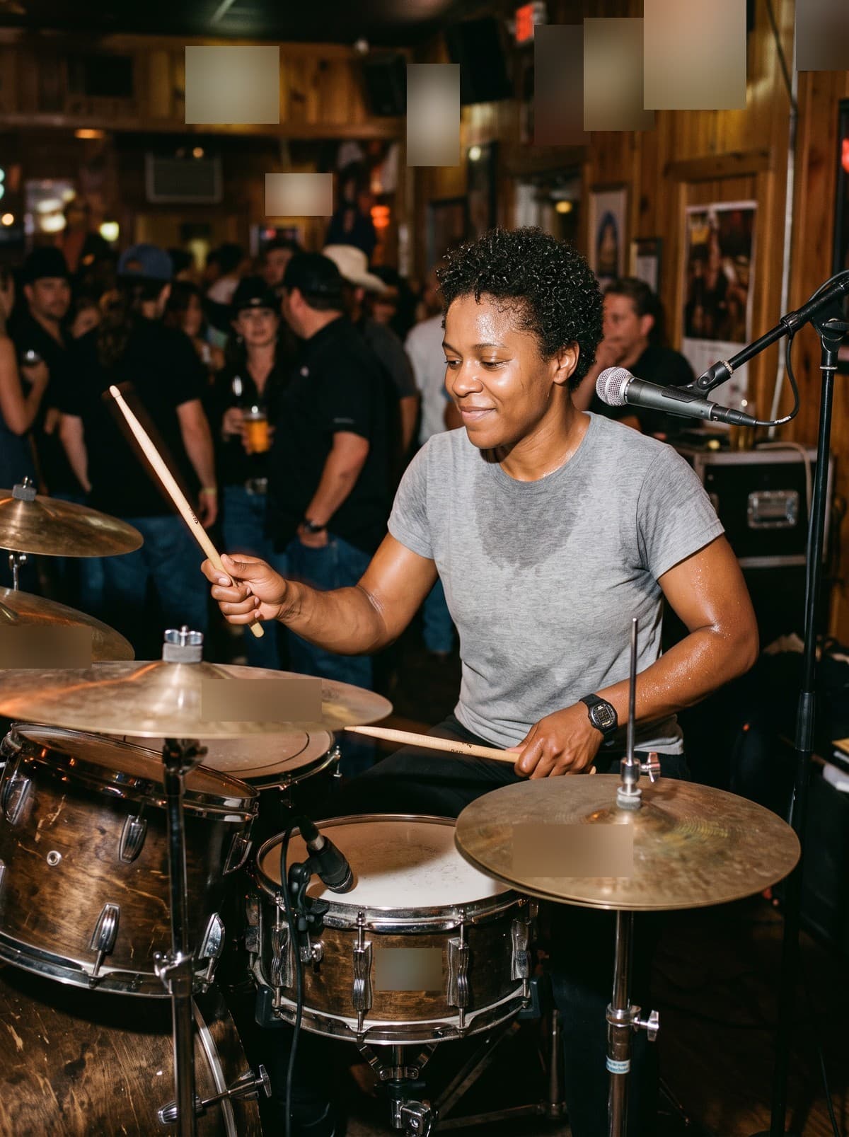 Wanda Pierce smiling at her drum kit in a crowded wood-panelled bar, mid-stroke